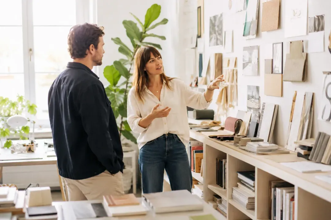 Two people discussing a client's project beside a wall of reference materials.